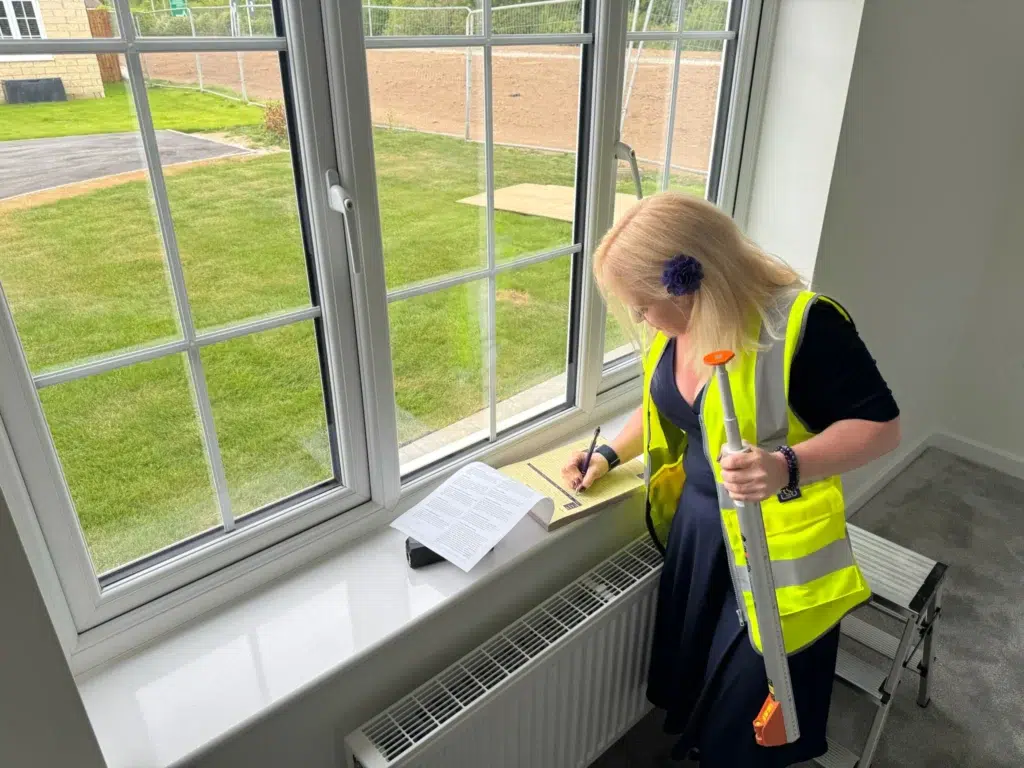 Ria in a hi-vis vest measuring a window in an unfinished new-build home and noting the sizes on the windowsill