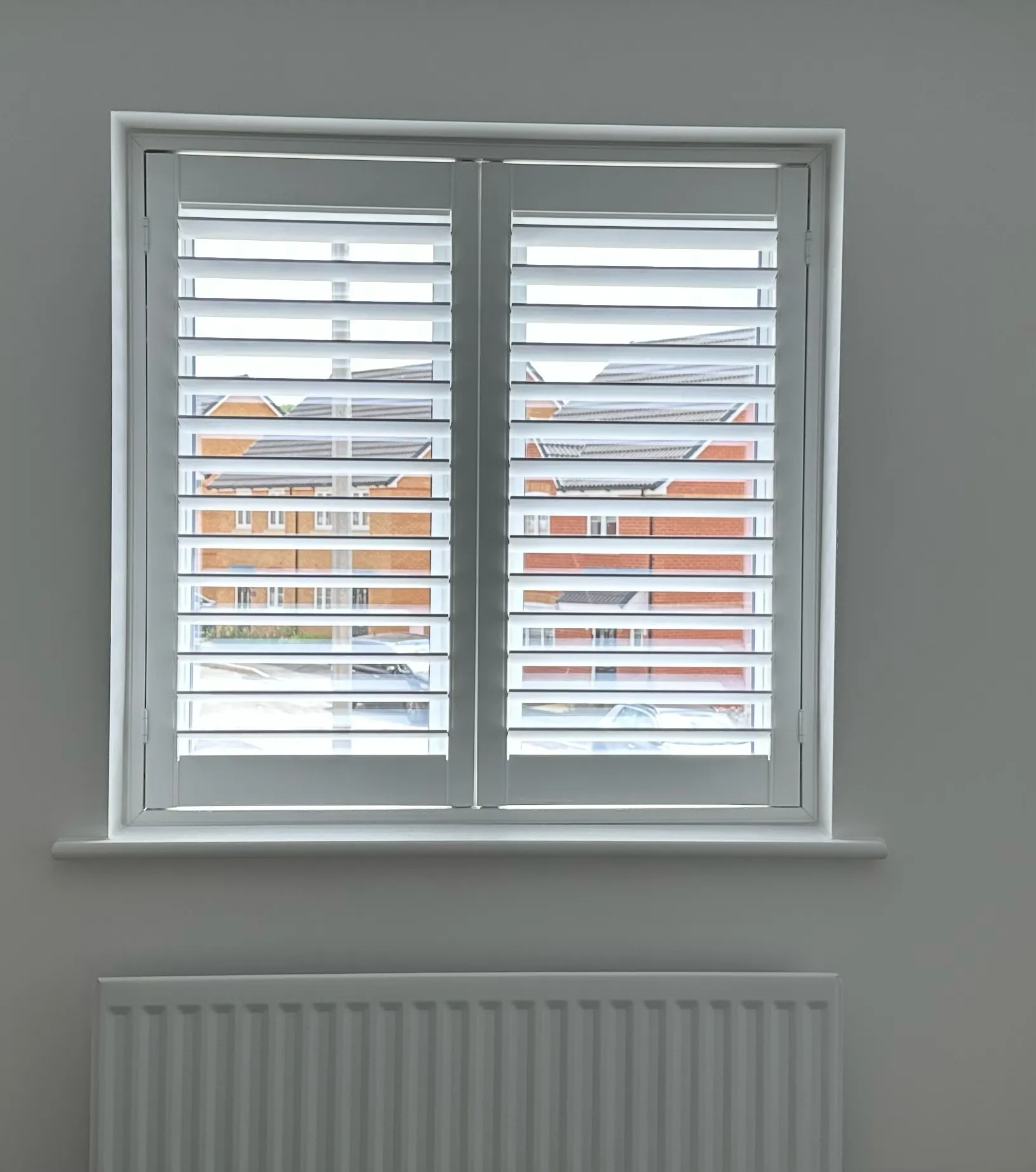 Completed white shutter installation above a radiator