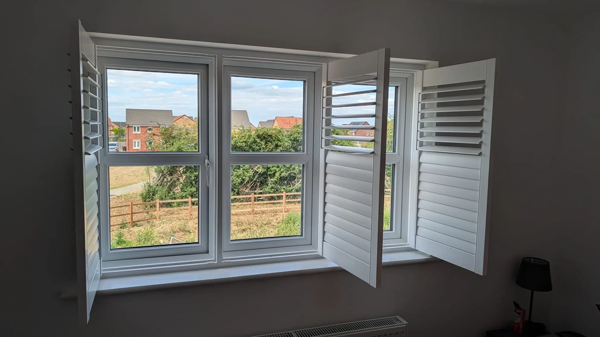 White made-to-measure shutters fitted to a wide bedroom window with the panels open