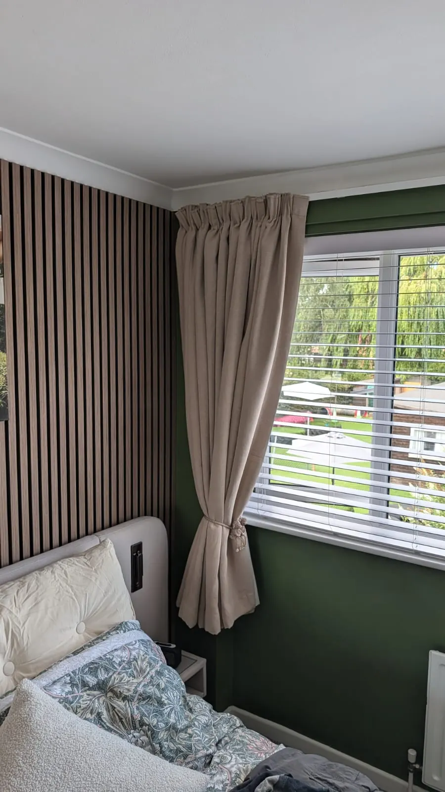 Close-up of pencil pleat curtains with a tieback beside a window with venetian blinds