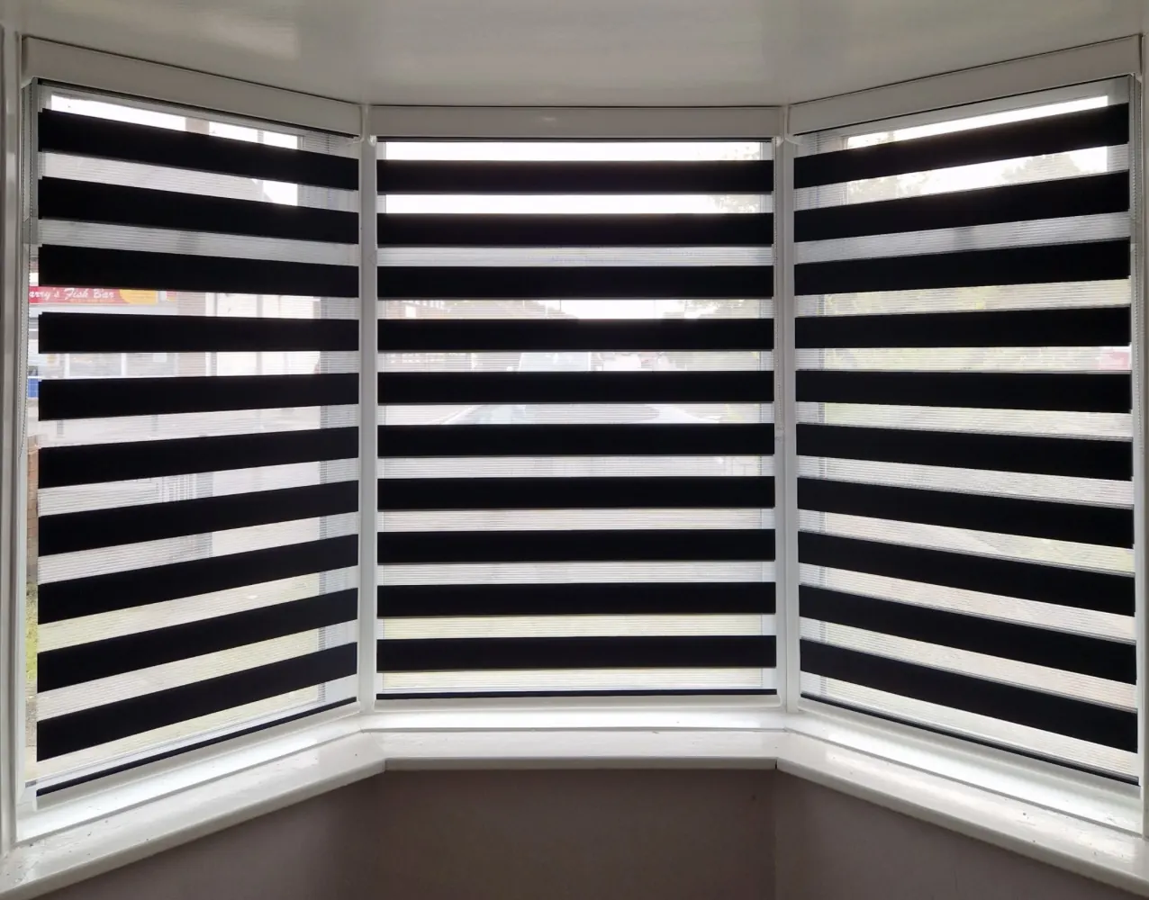 Black and white striped day and night blinds fitted across a three-section bay window