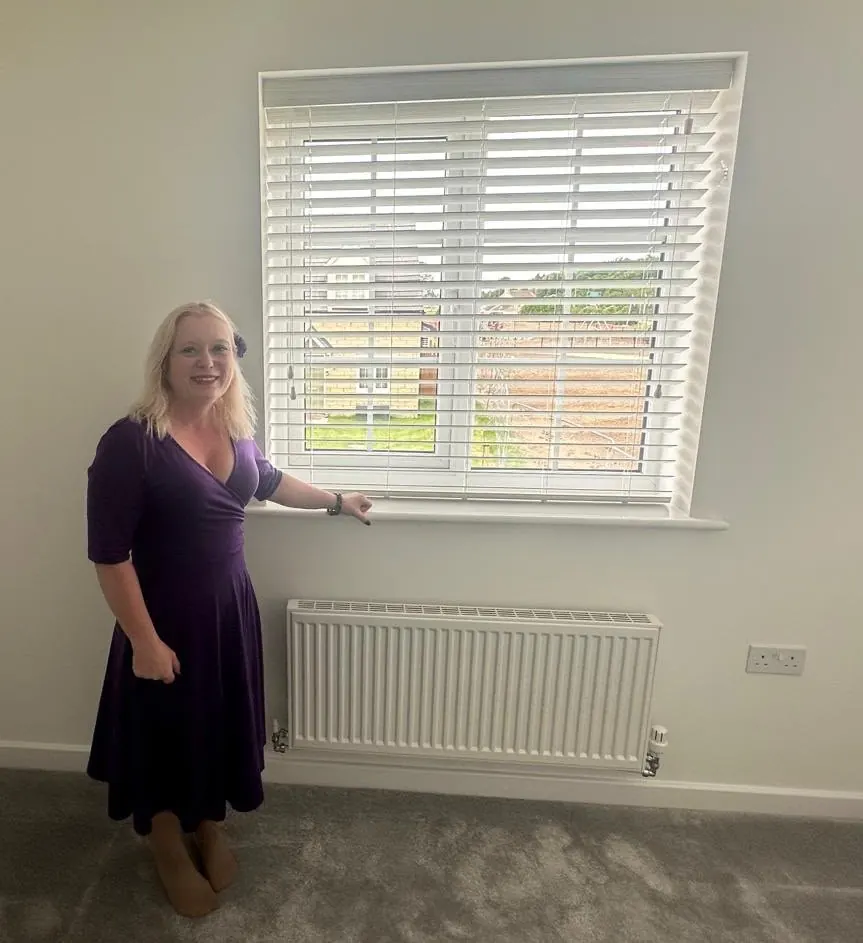 Ria beside a white Venetian blind fitted in a new-build bedroom