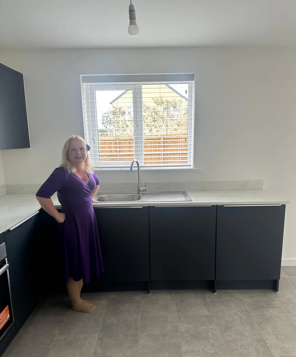 Ria beside a white Venetian blind fitted above a kitchen sink