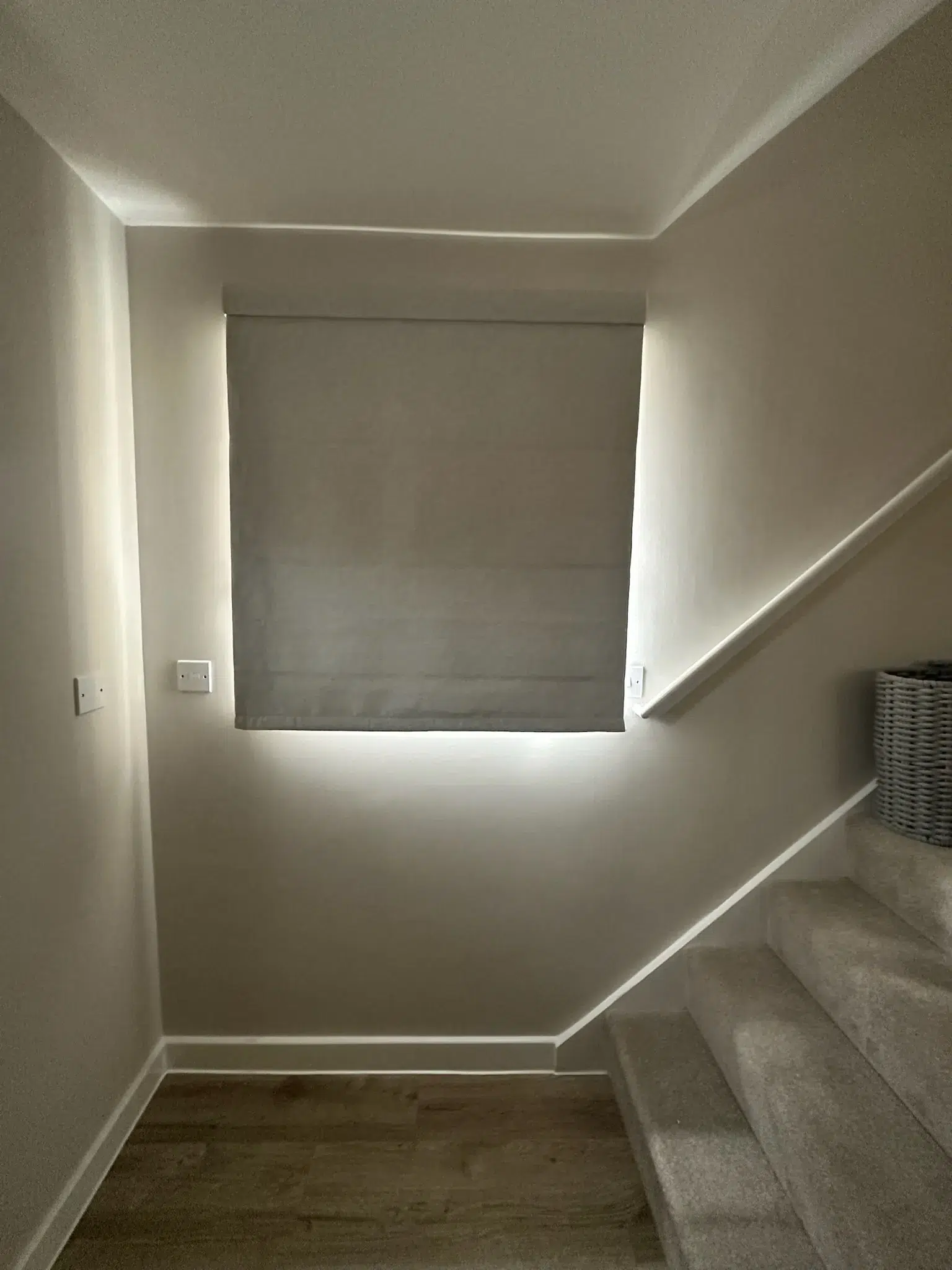 Grey Roman blind lowered over a staircase landing window
