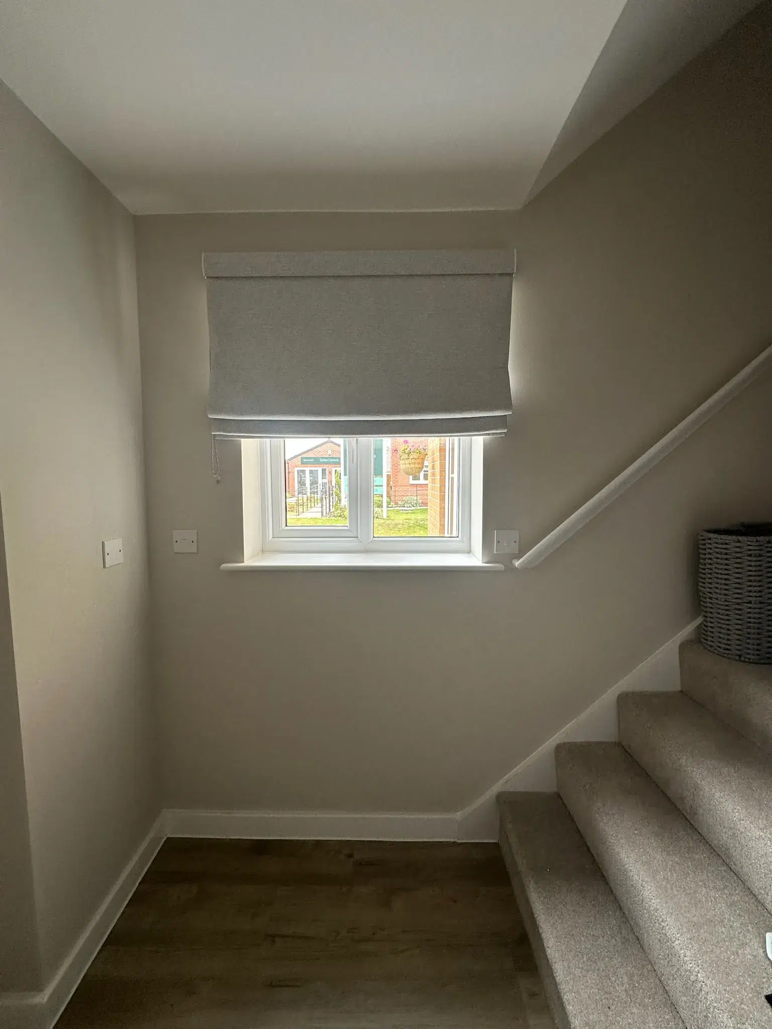 Grey Roman blind raised at a staircase landing window with the view visible