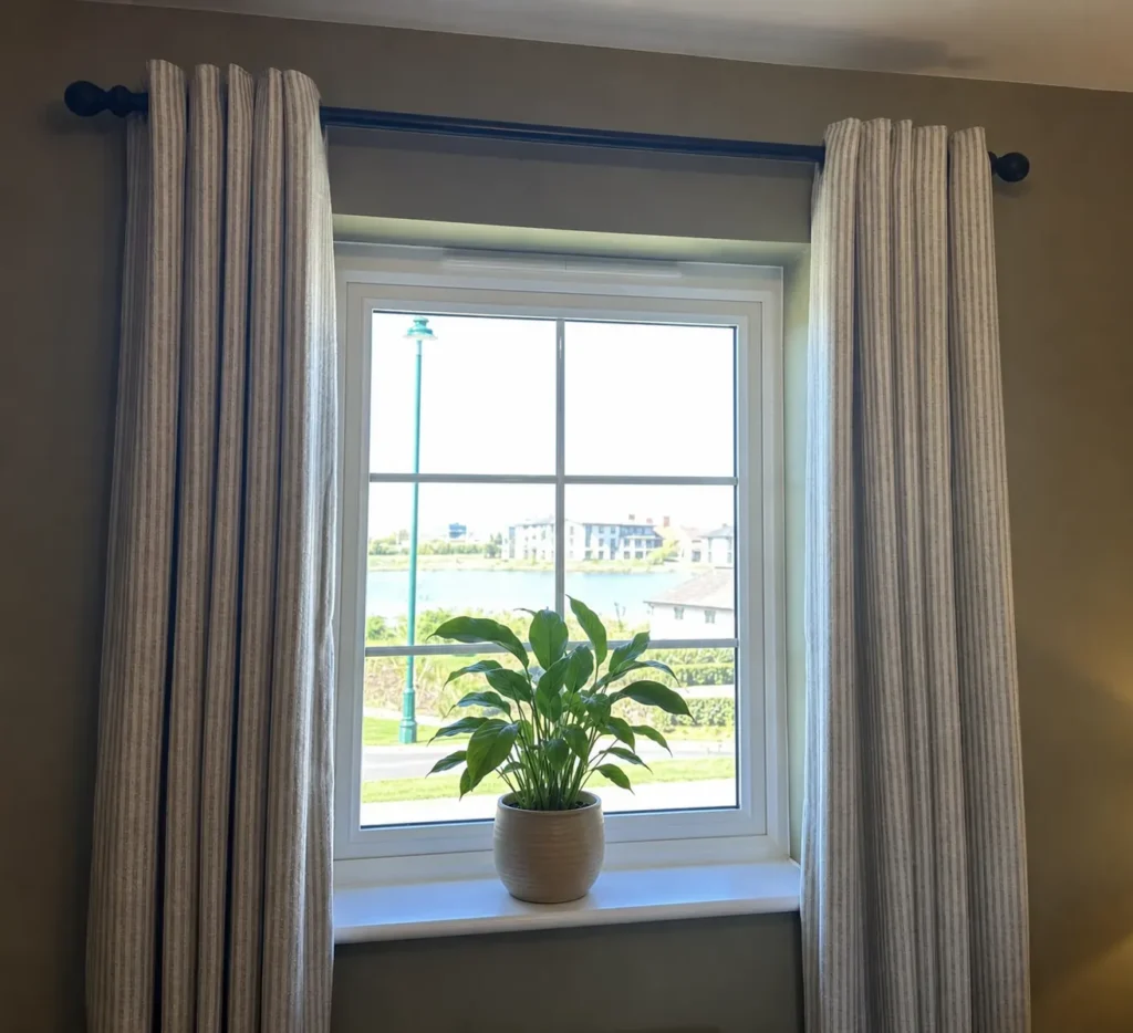 Striped linen curtains on a dark wooden pole framing a window with a lake view