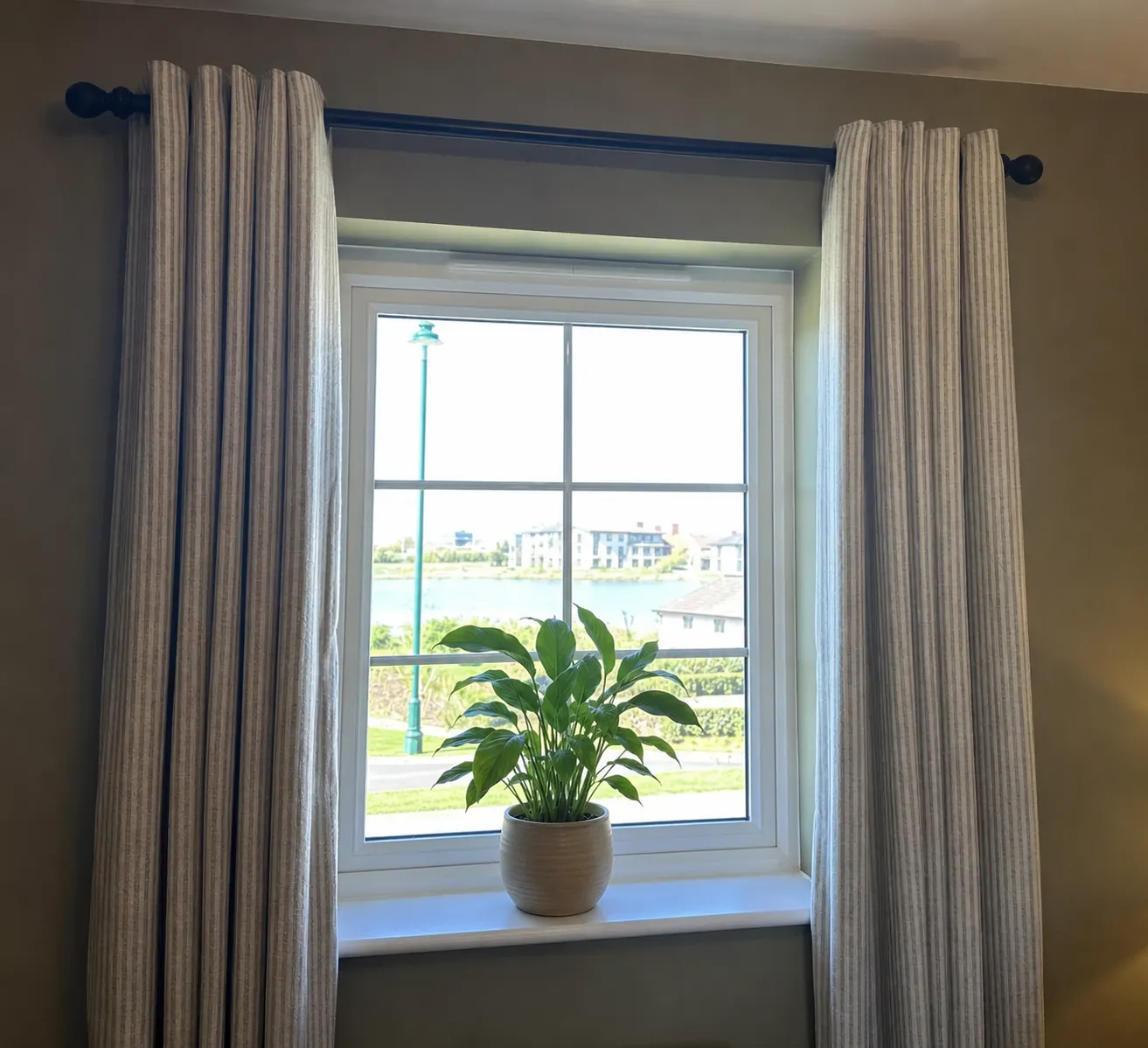 Striped linen curtains on a dark pole framing a window with a lake view