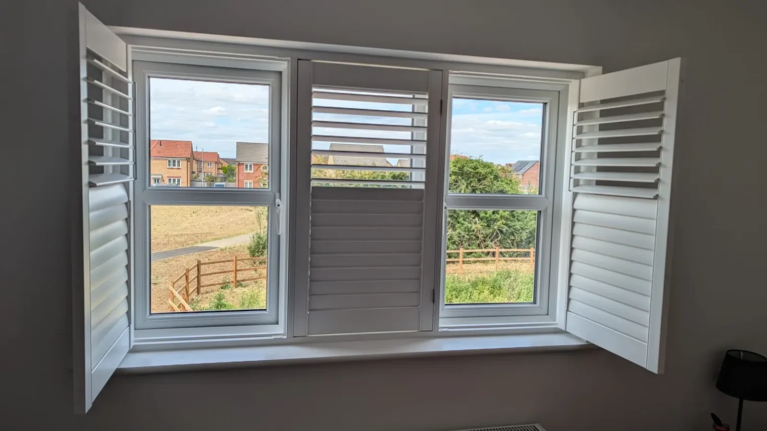 White UK-made shutters at a three-section window, with both side panels swung open and the centre panel closed