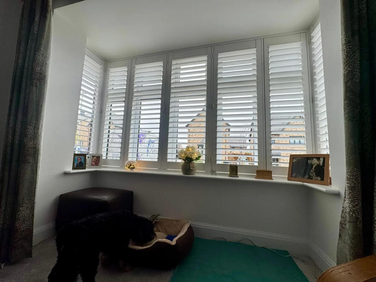 White UK-made seven-panel shutters fitted across a bay window in a living room
