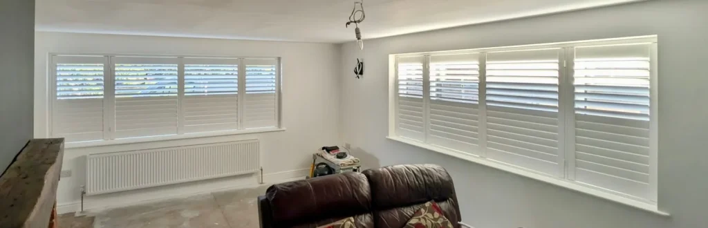 White UK-made shutters fitted across two wide lounge windows