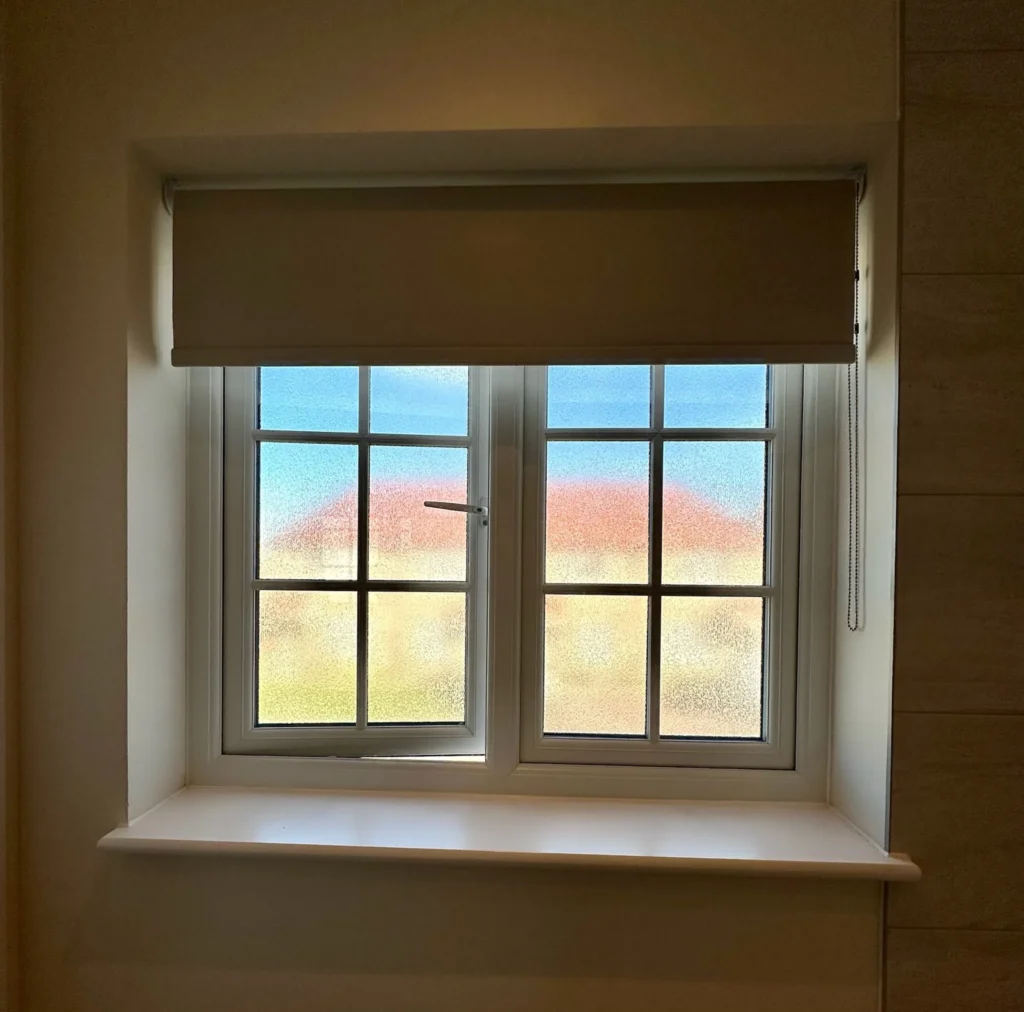 Neutral blackout roller blind fitted at a window with frosted glass