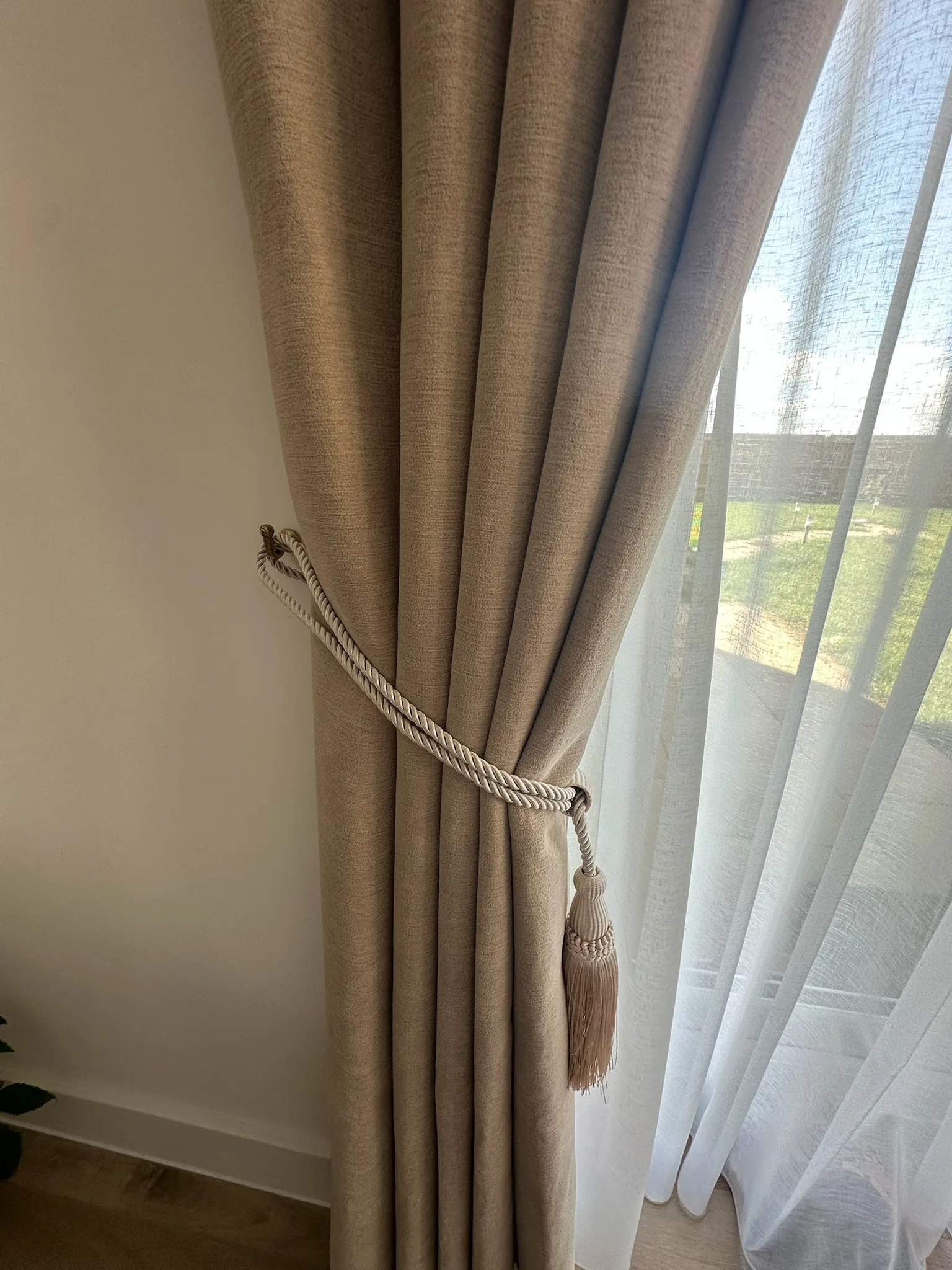 Close-up of a neutral made-to-measure curtain gathered with a rope and tassel tieback beside a sheer