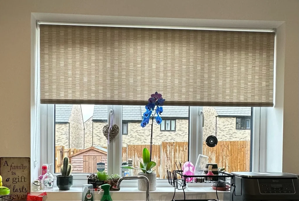 Natural woven roller blind fitted at a kitchen window above the sink