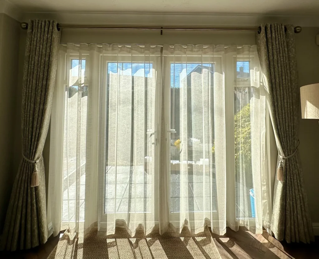 Patterned made-to-measure curtains held back with tiebacks, layered over wave voile sheers across garden doors