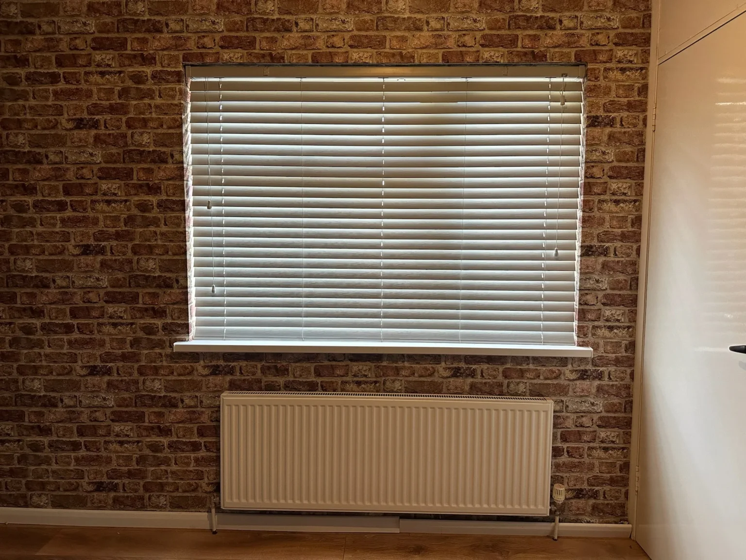 White Fauxwood Venetian blind fitted at a window in a brick-effect feature wall